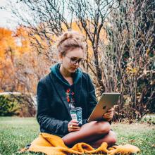 woman sitting in grass reading from a tablet