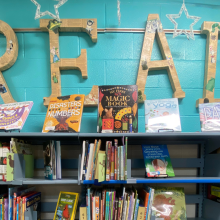 A school library bookshelf with various books and big sign that says, READ.