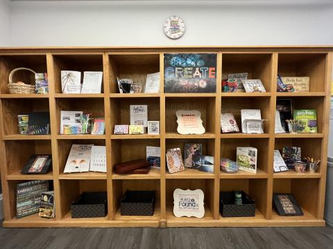 Wooden shelving unit with various craft supplies, books, and artwork.